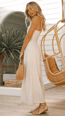Beige sleeveless jumpsuit with cinched waist, angled side view on a wooden deck.