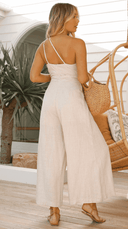Beige sleeveless jumpsuit with cinched waist, back angled view, on a patio.