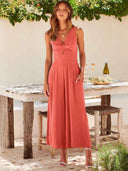 Coral wide-leg overall with V-neck, twisted bodice, and pockets, front view in outdoor setting.