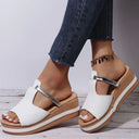 White platform wedge sandals with buckle ankle strap and two-tone tan flatform sole, worn with cropped jeans, angled side view.