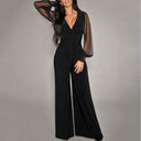 Black jumpsuit with sheer sleeves, V-neck, and studded cuffs, front view on gray background.