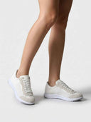 White mesh and suede lace-up sneakers worn on feet, angled view showing flexible outsole and lace-up closure.