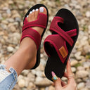 Red cushioned arch support sandals with wide mesh cross-strap and open-toe design, angled top view on stone surface.
