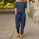 Navy two-piece jumpsuit set with short-sleeve top and tie-waist pants, front view on a brick path.