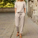 Light beige two-piece jumpsuit set with short-sleeve top and tie-waist pants, front view on a street.