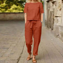 Rust two-piece jumpsuit with short-sleeve top and tie-waist pants, front view on a brick path.