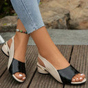 Two-tone low wedge sandal in black croc-embossed upper and cream slingback strap, peep-toe open front, angled side view on foot.