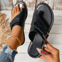 Black leather flat toe-ring sandal with buckle cross-strap and contrast stitching, angled overhead view on light background.