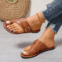 Tan brown leather flat toe-ring sandal with buckle strap and contrast stitching, angled view on model wearing distressed denim.