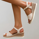 Beige espadrille wedge sandals with adjustable ankle strap worn on foot, angled side view showing jute wedge heel and white rubber outsole.