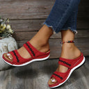 Red mesh platform slide sandals with black wave embroidered trim and tan cushioned footbed, angled front view on wooden deck.