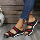 Black mesh platform slide sandals with red embroidered wave trim and white rubber sole, angled side view on wooden deck.