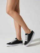Black canvas court trainers with white laces and flat white sole, angled view on light background.
