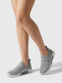 Grey sparkle-knit slip-on trainers with elasticated strap and white sole, shown on feet from an angled view.
