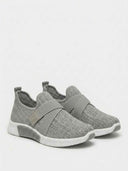 Pair of grey slip-on knit trainers with rhinestone-effect upper, elastic midfoot strap, and white outsole — angled view.