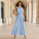 Light blue pleated halter-neck jumpsuit with tie waist, full front view in an arched walkway.