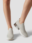 Light grey slip-on knit trainer with metallic silver heel counter, angled view on white background.