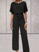 Black short sleeve jumpsuit with adjustable cinch belt, front view on a light textured background.