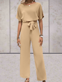 Tan short sleeve jumpsuit with adjustable cinch belt, front view on a light textured background.