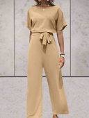 Tan short-sleeve jumpsuit with a cinched waist tie, front view on a light textured background.