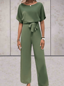 Green short sleeve jumpsuit with cinch belt, front view on a light textured background.