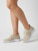 Beige cushioned knit trainers with arch support worn on a model's feet, angled view showing sole profile.