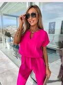 Hot pink jumpsuit with keyhole neckline, tie waist, and cuffed sleeves, front view.