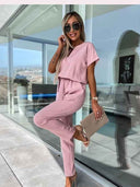 Pink short-sleeve jumpsuit with V-neck, cinched waist, and straight legs, angled view.