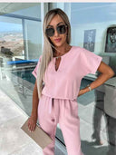 Pink short-sleeved jumpsuit with V-neck, tie waist, and cuffed sleeves, front view.