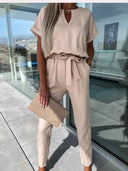 Beige jumpsuit with V-neck, short sleeves, and waist tie, front view on a patio.