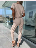 Beige jumpsuit with short sleeves and elastic waist, back view on a modern patio.