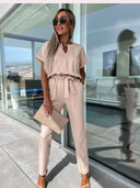 Beige V-neck jumpsuit with short sleeves and waist tie, worn by a model outdoors.