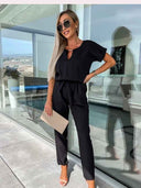 Black short-sleeve jumpsuit with V-neck cutout, front view on a patio.