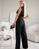 Black V-neck jumpsuit with tassel tie belt, angled back view in a living room.