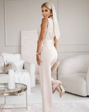 Pale pink V-neck jumpsuit with tassel tie belt, angled back view in a living room.