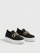 Platform slip-on trainer in black showing side profile, chunky white sole and gold chain ornament.