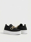 Close-up detail of gold curb-chain hardware on black knit platform slip-on trainer.