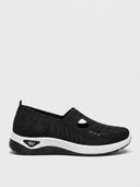 Black knit slip-on trainers with T-bar cut-out detail, perforated toe zone and white chunky sole, side view.