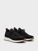 Black knit mesh trainers with white midsole, gum outsole, and red heel pull-loop visible at the heel, angled view.