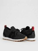 Black mesh trainers with suede-look side panel overlays, white midsole, gum rubber outsole, and red heel tab, close angled view.