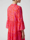 Red mini dress with pink tropical print, tiered skirt, and ruffled sleeves, back angled view.